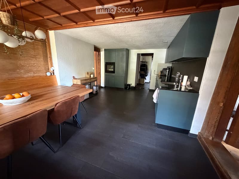 Open-plan kitchen and dining area with dark flooring, wooden dining table, brown chairs, kitchen island, and modern appliances.