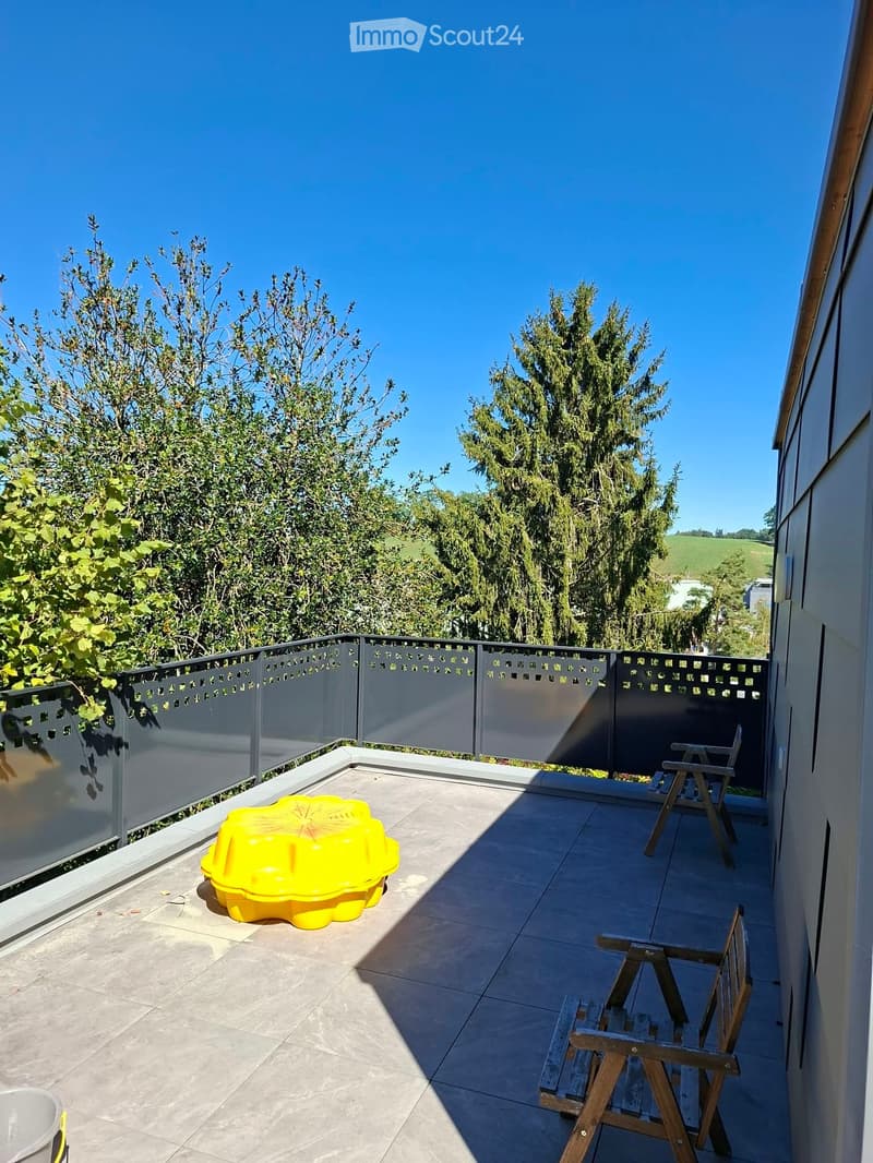 Balcony with tiled floor, metal railing, two wooden chairs, and a yellow plastic container.