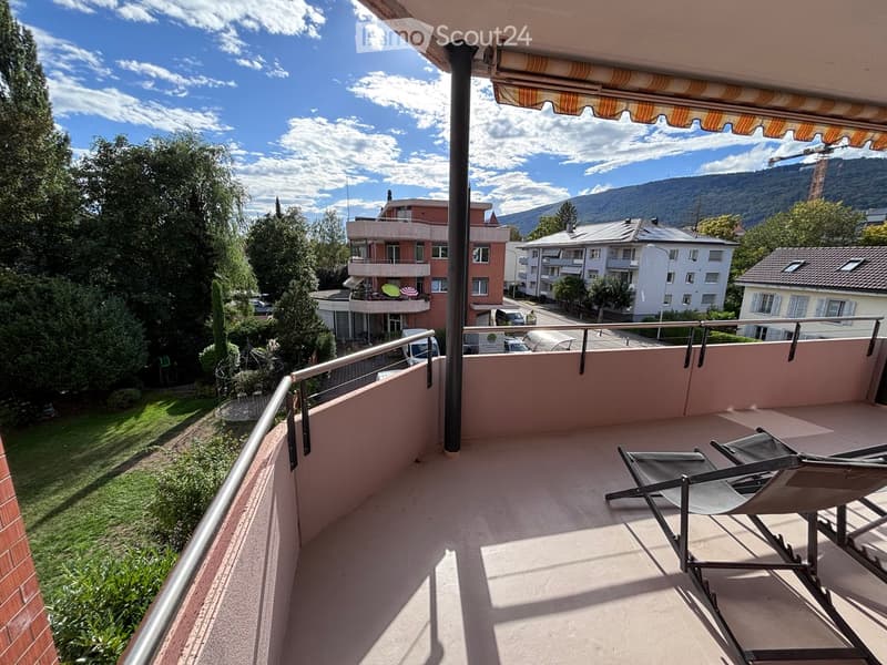 Balcony with a view of the surrounding area, including buildings and greenery, with a single chair placed on the floor.