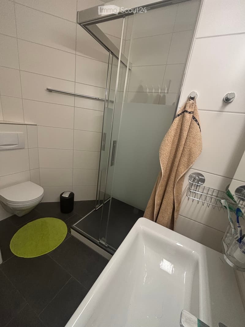 Modern bathroom with a bathtub, toilet, glass-enclosed shower, towel, toothbrush holder, and a green bath mat.