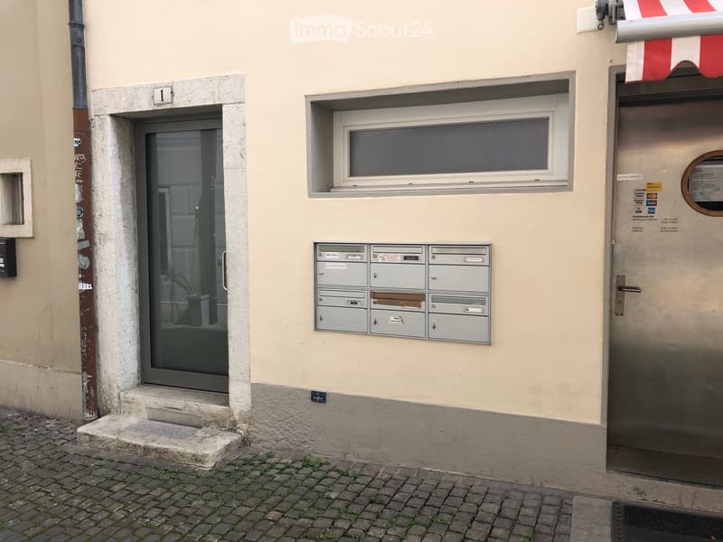 Exterior view of a building entrance with a glass door, mailboxes, and a small window above the door.