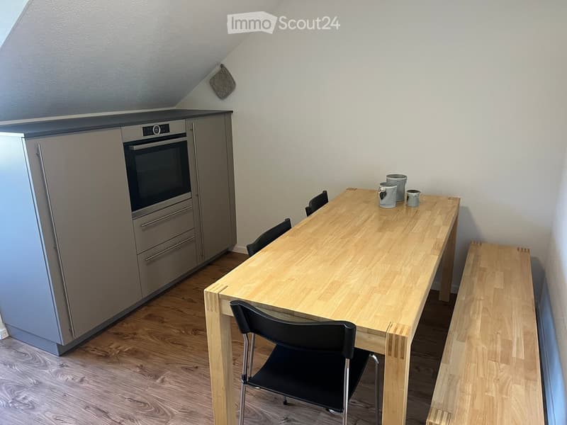 Modern kitchen with light wood flooring, built-in refrigerator, oven, and a wooden dining table with chairs and cups.