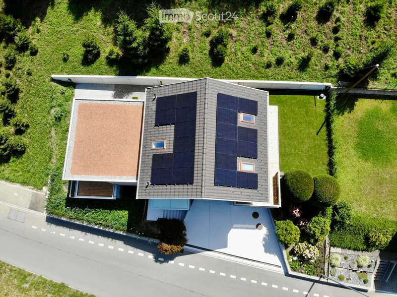 A modern two-story house with solar panels on the roof, surrounded by a well-maintained garden and lawn.