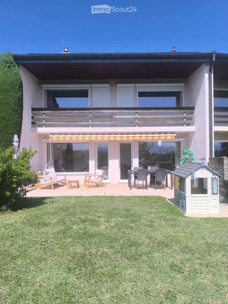 Well-maintained garden with a lawn, patio area with chairs and a table, and a small playhouse.