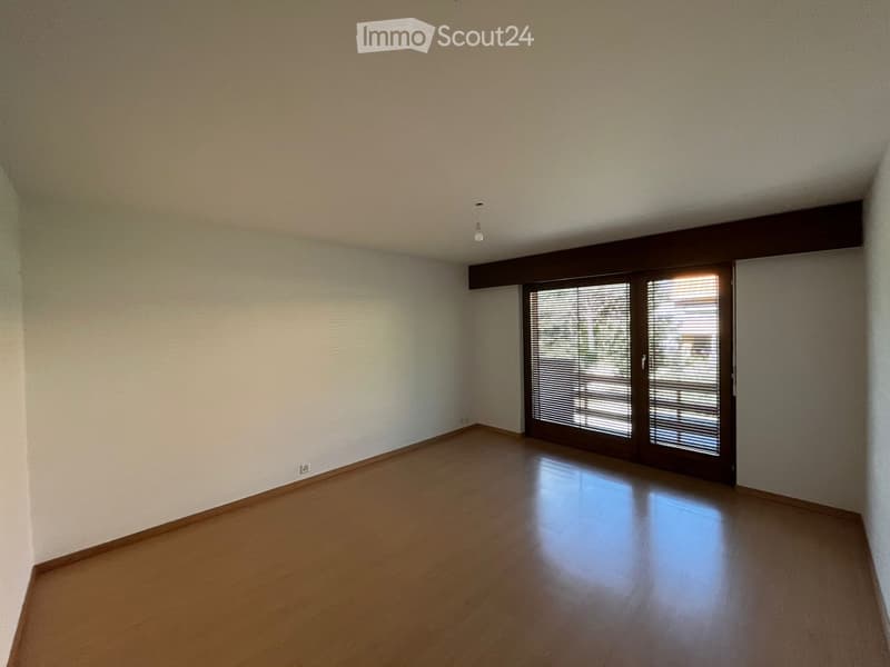Empty room with wooden flooring, white walls, and large sliding glass doors with blinds.