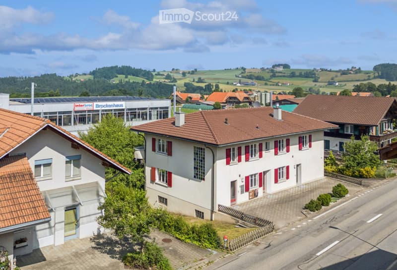Aerial view of a residential area with multiple houses, red-tiled roofs, and surrounding greenery.