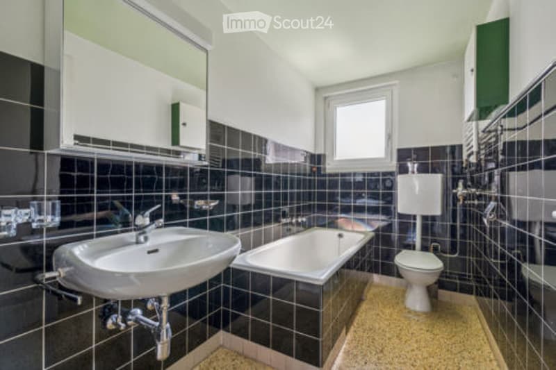 Modern bathroom with black tiled walls, white fixtures, and a large window for natural light.