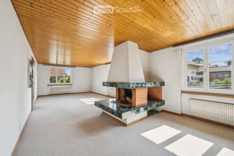 Empty room with wooden ceiling, fireplace, large windows, and light-colored carpeting.
