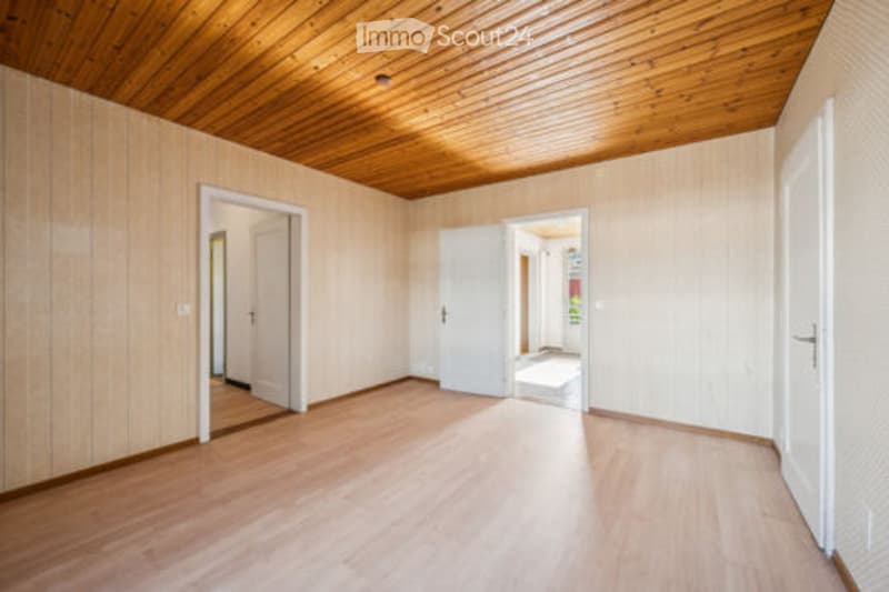 Empty room with wooden flooring and paneled walls, featuring multiple doors leading to adjacent spaces.