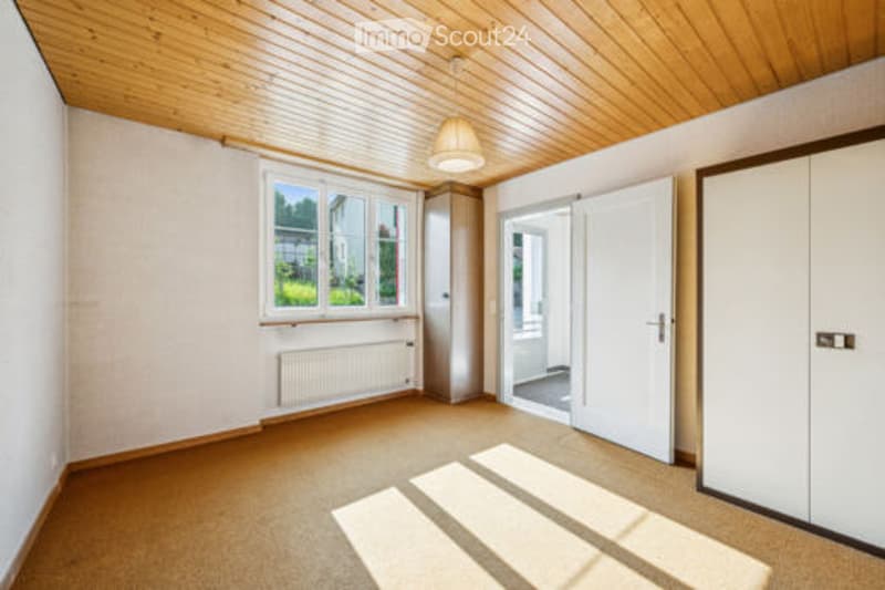 Empty room with wooden ceiling, white walls, large window, radiator, and built-in wardrobe.