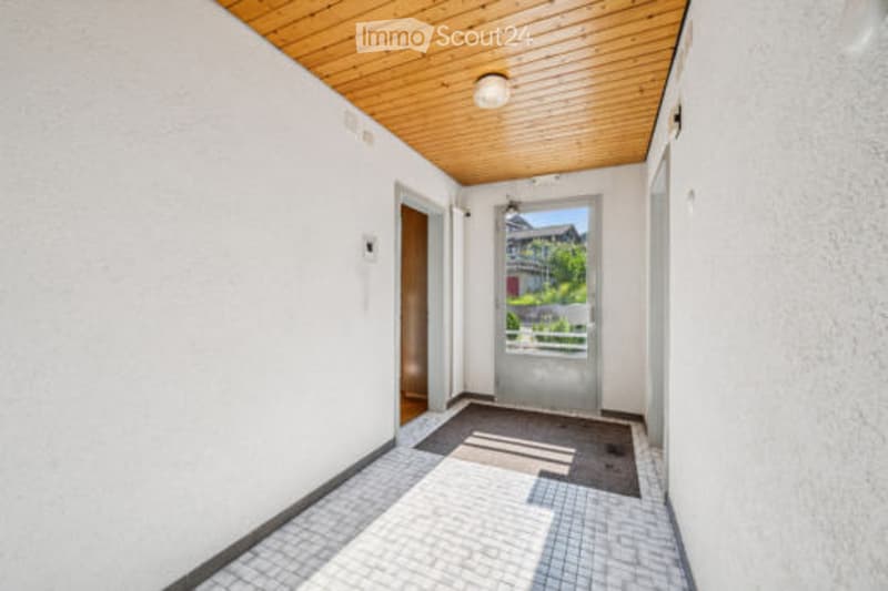 Bright hallway with white walls, wooden ceiling, tiled floor, and a door leading to an outdoor area.