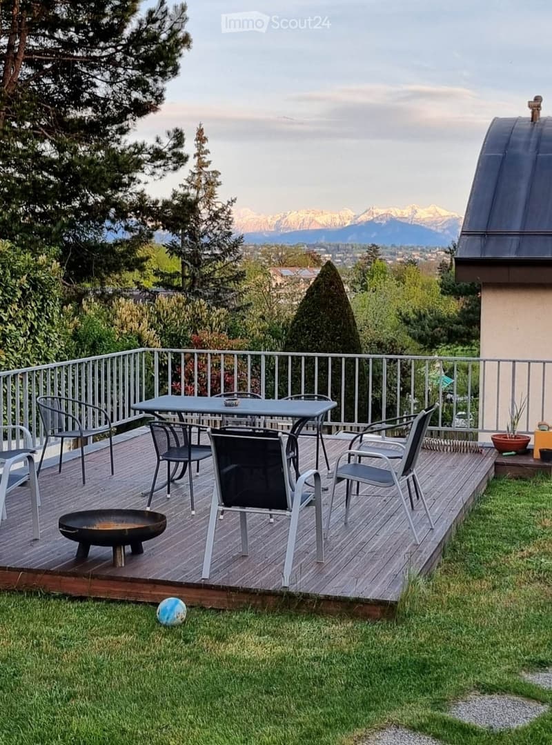 Wooden deck with a metal railing, a table with chairs, a fire pit, and a view of mountains and trees.