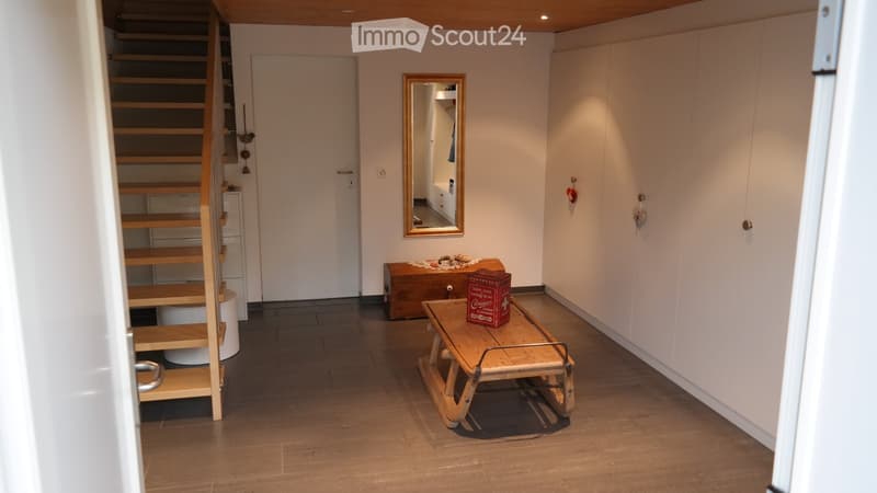 Hallway with wooden floor, bench, mirror, and small table with items on it.