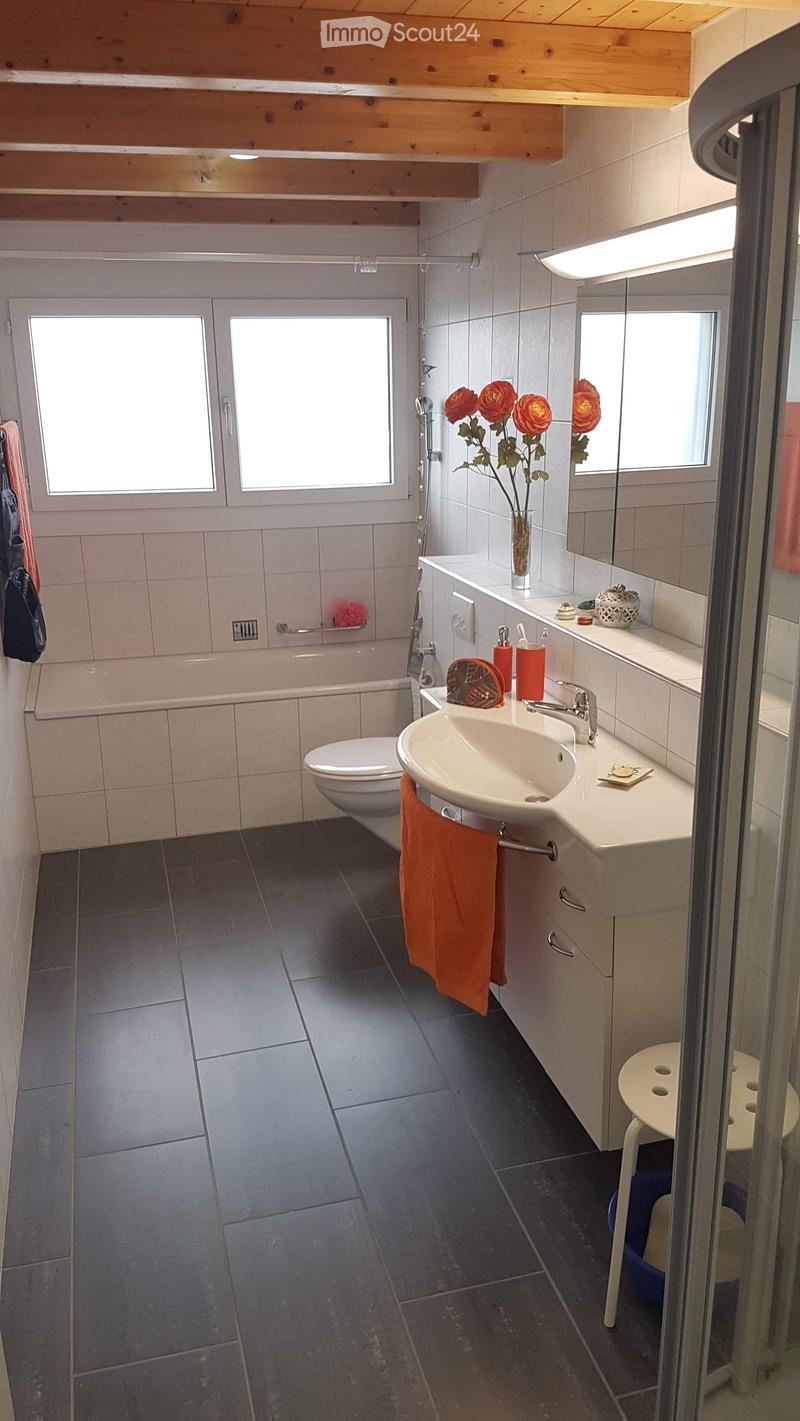 Modern bathroom with dark tiled floor, white sink, toilet, bathtub, and a small white stool near the shower area.