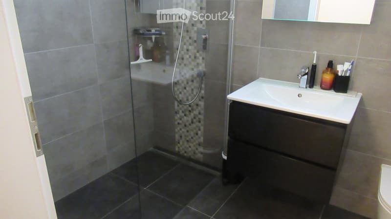 modern bathroom with glass shower, white sink, black cabinet, tiled floor, mirror