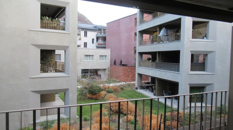 Apartment building with multiple balconies, garden area, and a view of the mountains