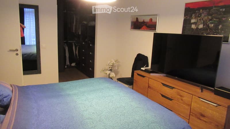 Bedroom with bed, wooden dresser, TV, flowers, closet, mirror, and framed pictures on the wall.