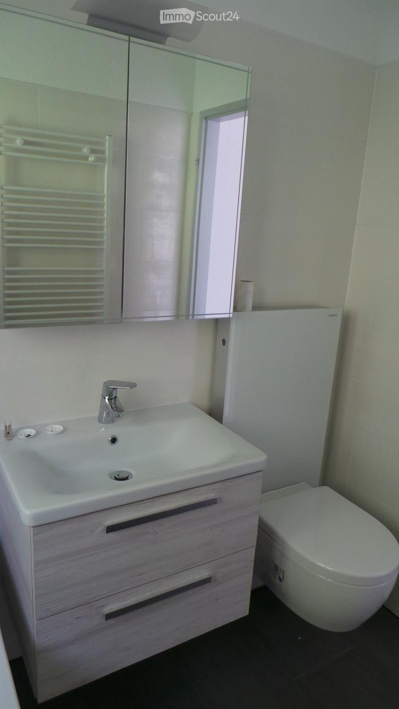 Modern bathroom with a white sink, chrome faucet, mirrored cabinet, and toilet. Light-colored tiles and a sleek design.