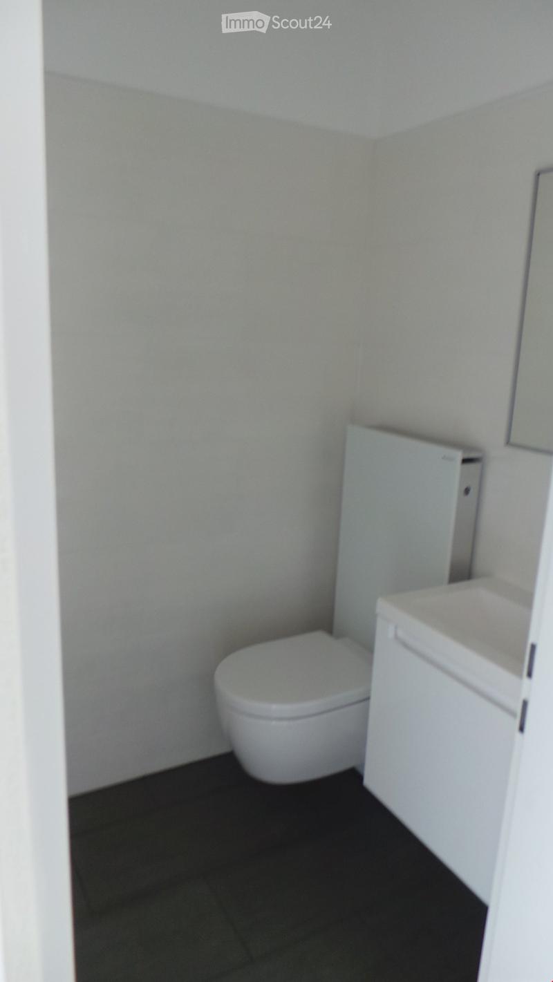 A compact bathroom with a toilet, a sink, and a white cabinet. The walls are light-colored, and the floor is dark.