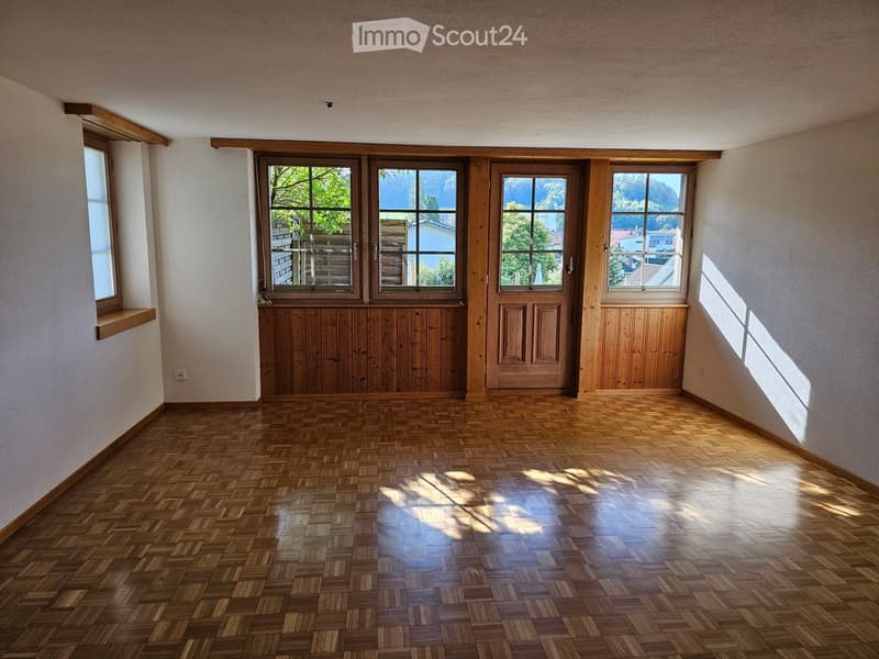 Empty room with wooden herringbone flooring, large windows with wooden frames, and white walls.