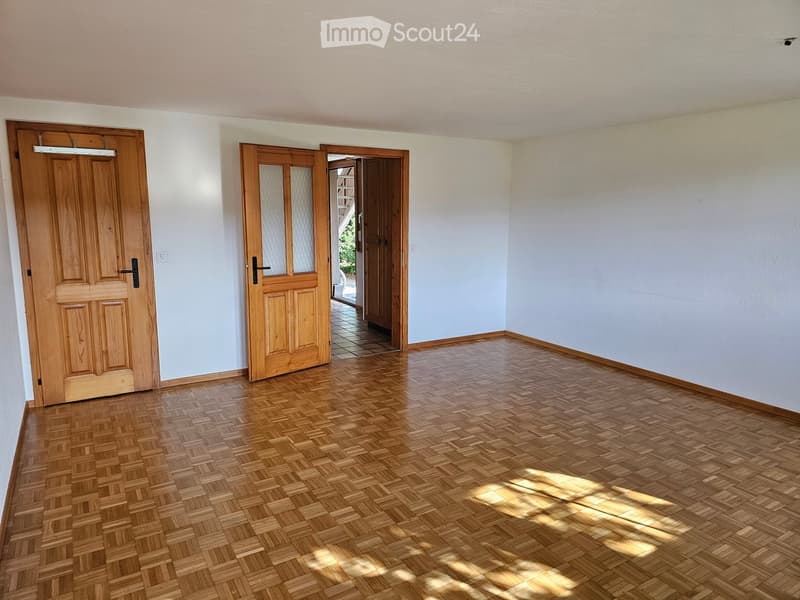 Empty room with wooden parquet flooring, light-colored walls, and two wooden doors leading to other spaces.