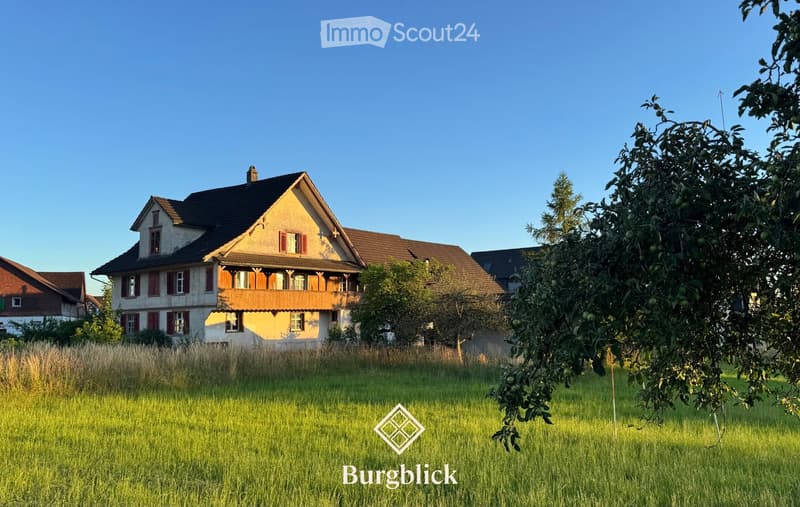 A two-story house with a wooden balcony, red shutters, and a well-maintained lawn in front.