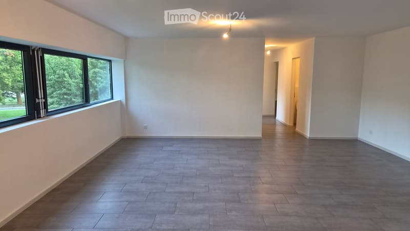 Empty room with grey tiled floor, white walls, large window with black frame, and visible electrical outlets.