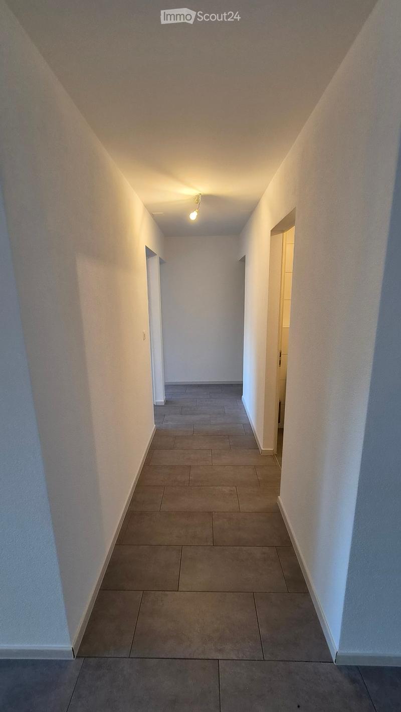 Empty hallway with tiled floor, white walls, and recessed lighting. Two doorways lead to adjacent rooms.