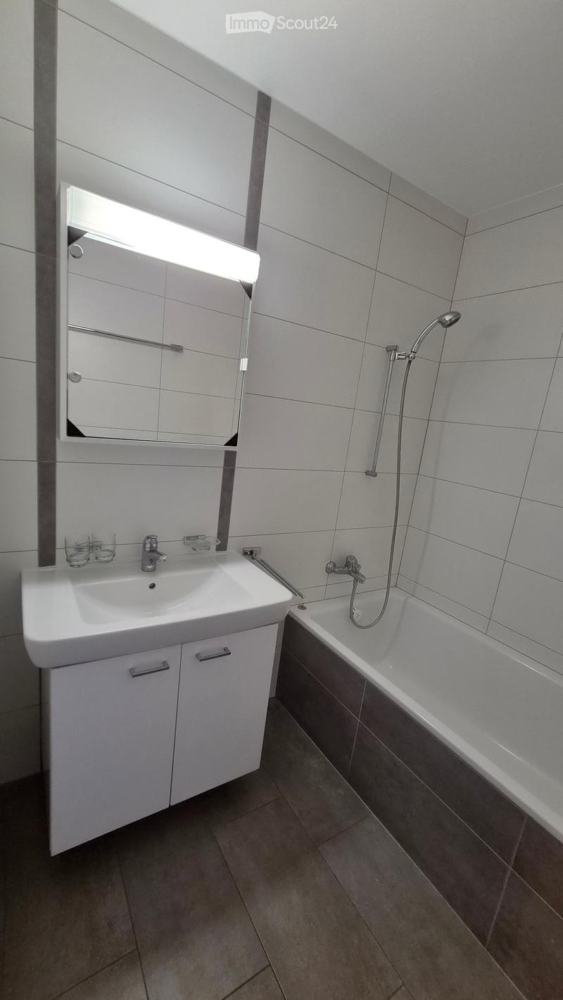 Modern bathroom with a white sink, bathtub, mirror, and two cups on the sink counter.