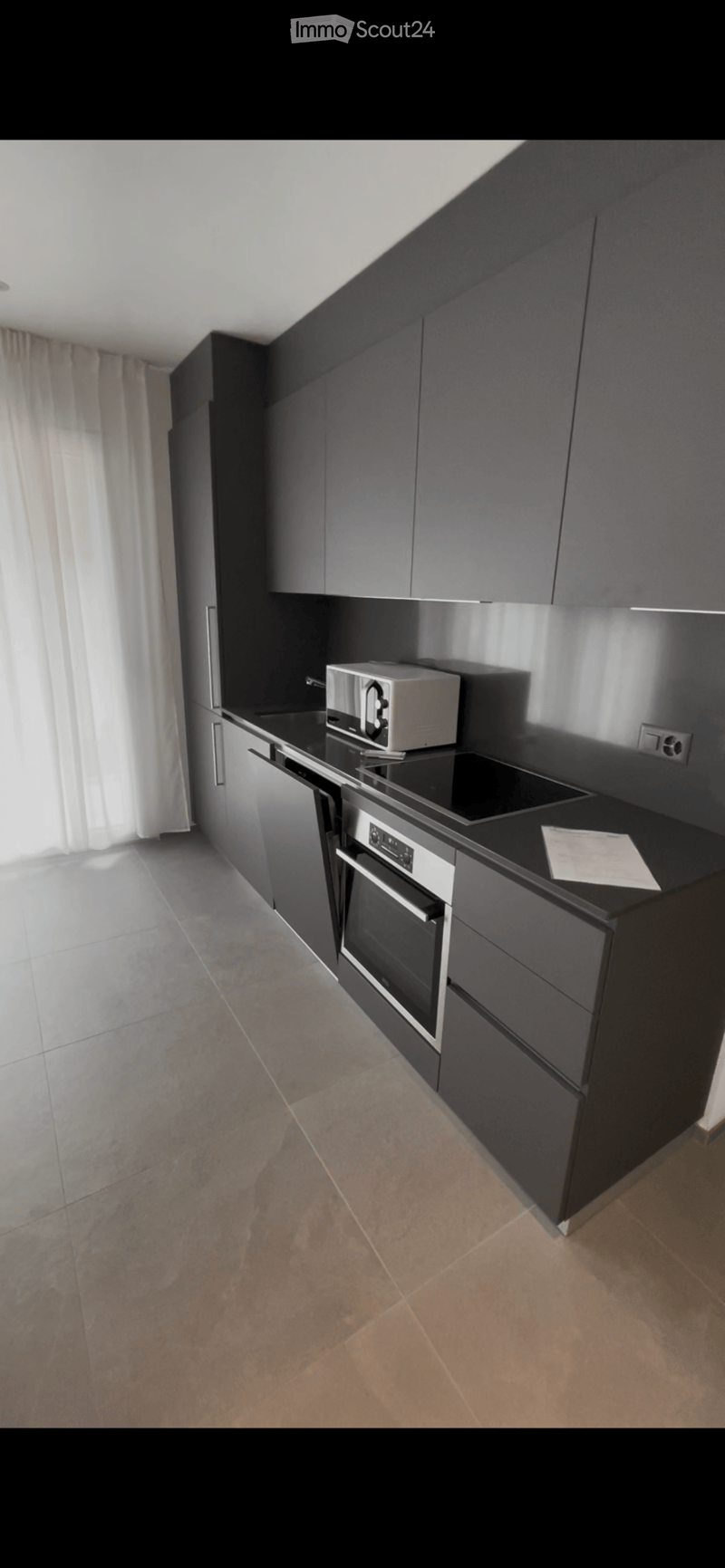 Modern kitchen with dark grey cabinets, stainless steel appliances, and a black countertop. Features an oven, microwave, and a small piece of paper on the counter.