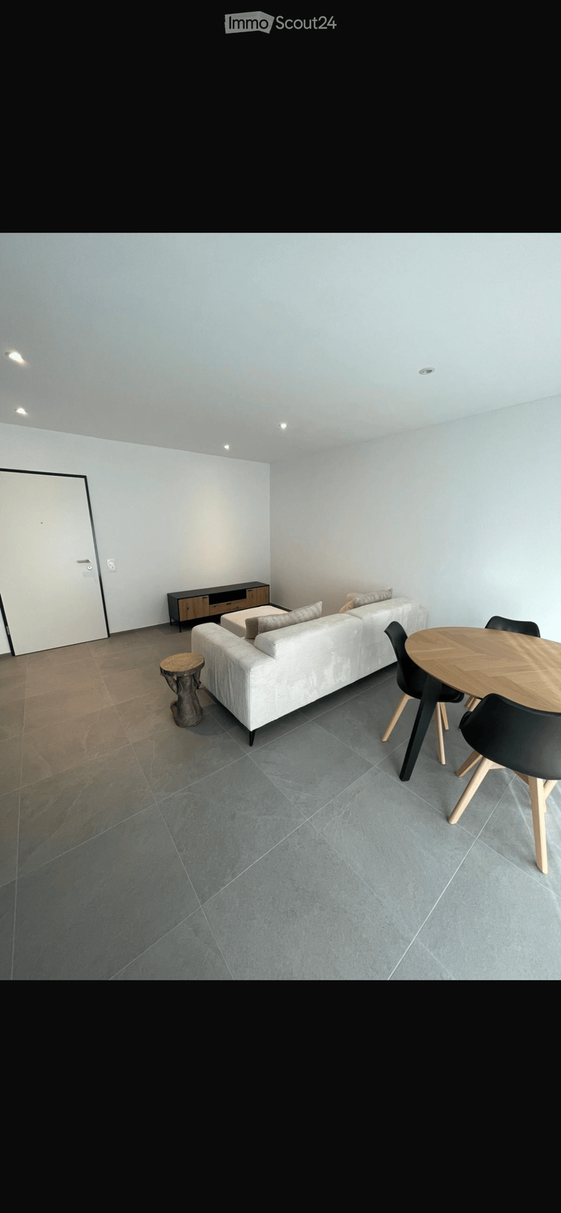 Modern living room with a grey sofa, coffee table, wooden stool, and dining table with chairs.