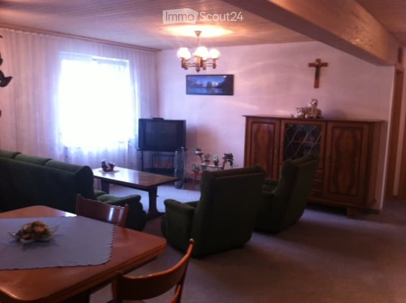 A cozy living room with a green sofa, armchairs, coffee table, TV, wooden cabinet, and a dining area with a table and chairs.