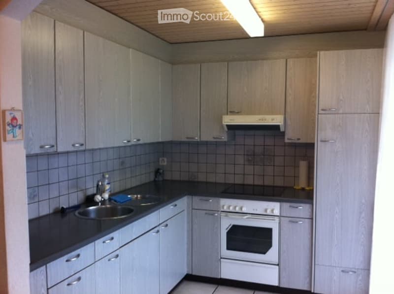 Modern kitchen with light grey cabinets, black countertops, stainless steel sink, and built-in oven and range hood.