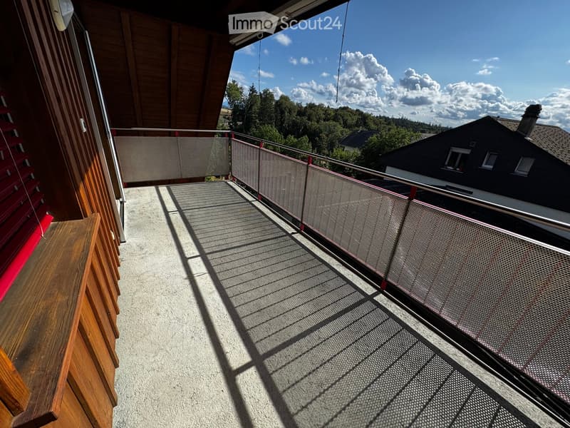 Balcony with metal railing, wooden steps, and a view of the surrounding landscape and neighboring house.