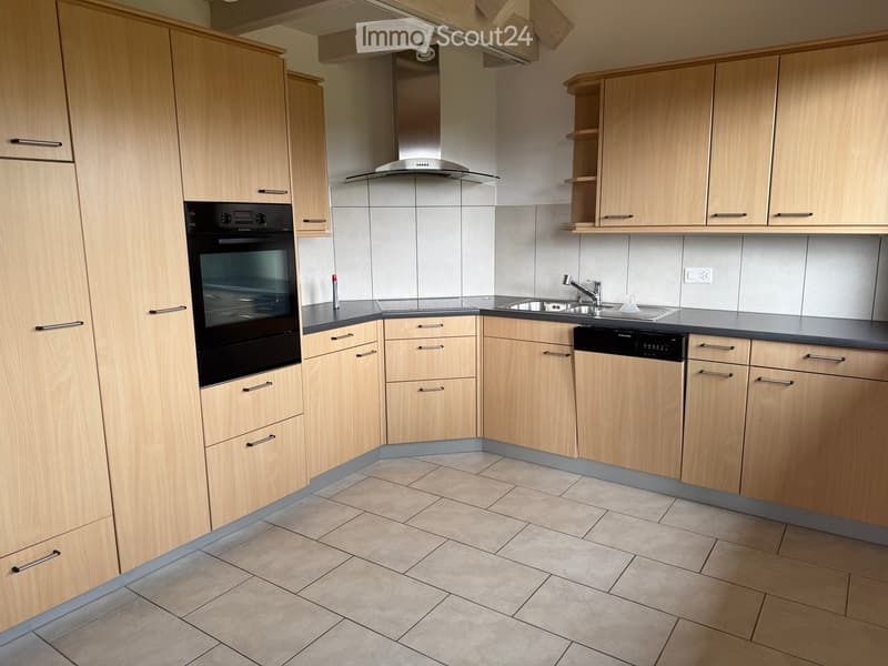 Modern kitchen with light wooden cabinets, stainless steel appliances, tiled floor, and black countertops.