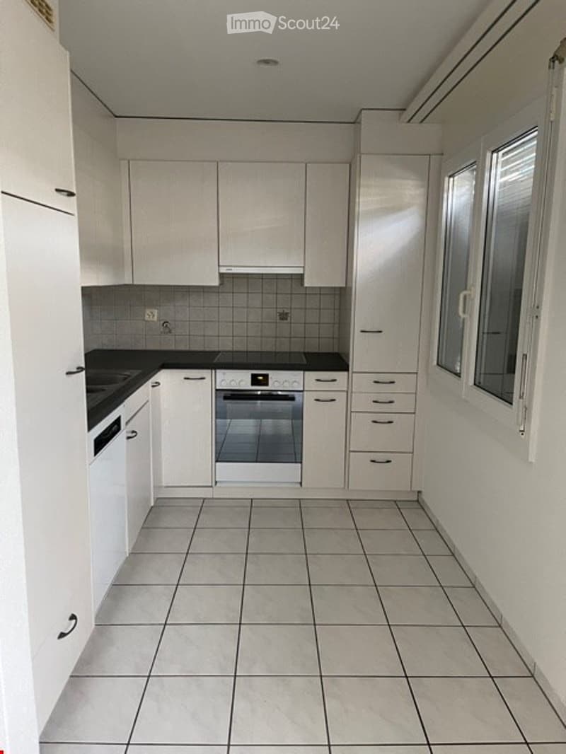 Modern kitchen with white cabinets, tiled floor, and built-in appliances including an oven and dishwasher.