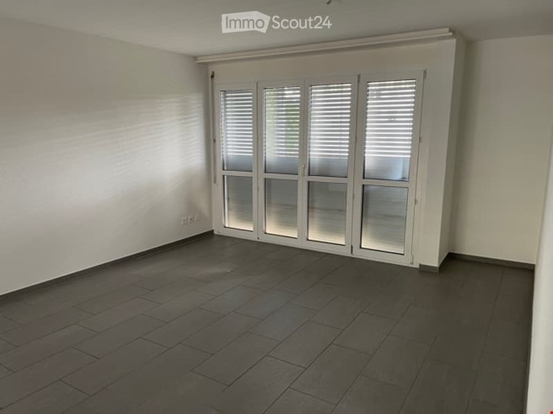 Empty room with dark wooden flooring, white walls, and large white sliding doors with blinds.