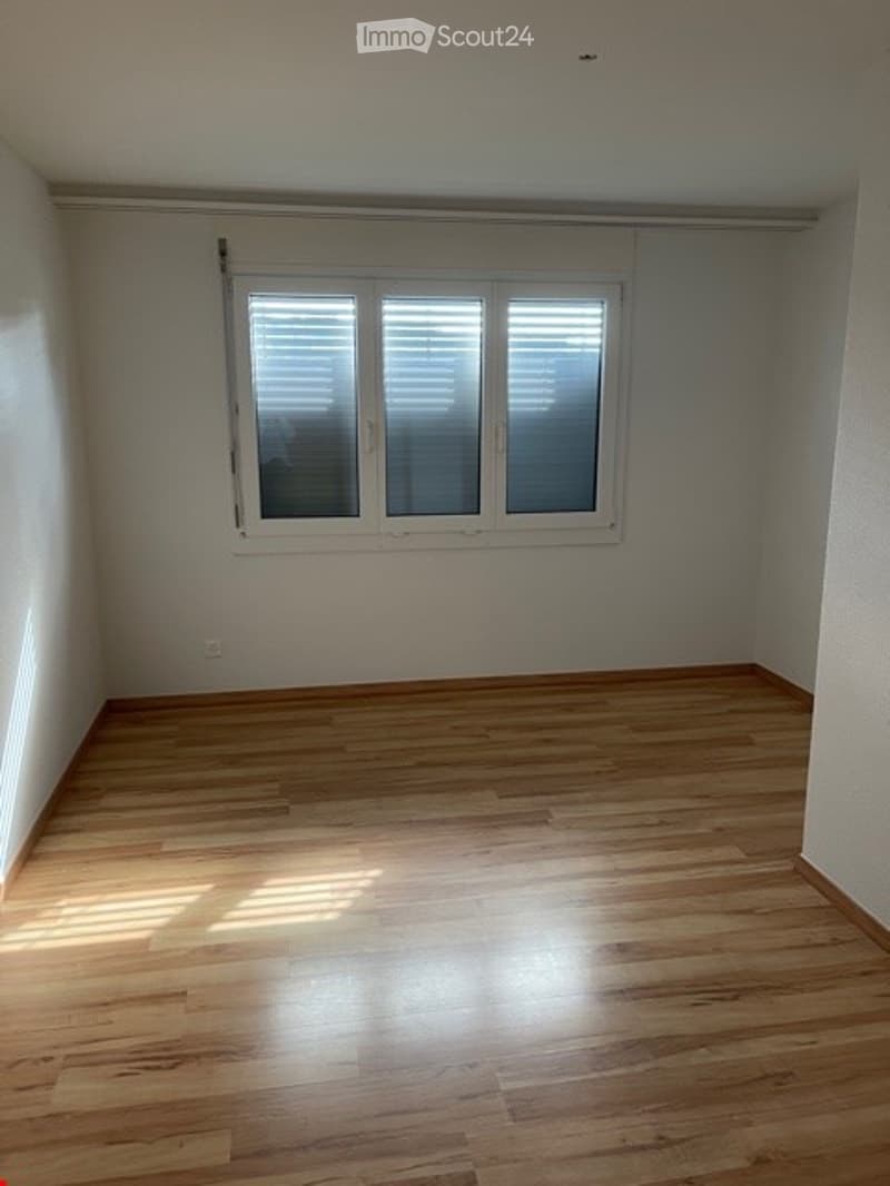 Empty room with wooden flooring and a large window with blinds, no furniture or equipment.