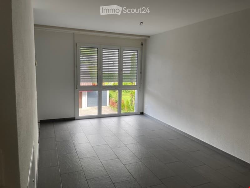 Empty room with tiled floor, large sliding glass door leading to outdoor area, white walls, and bright natural light.
