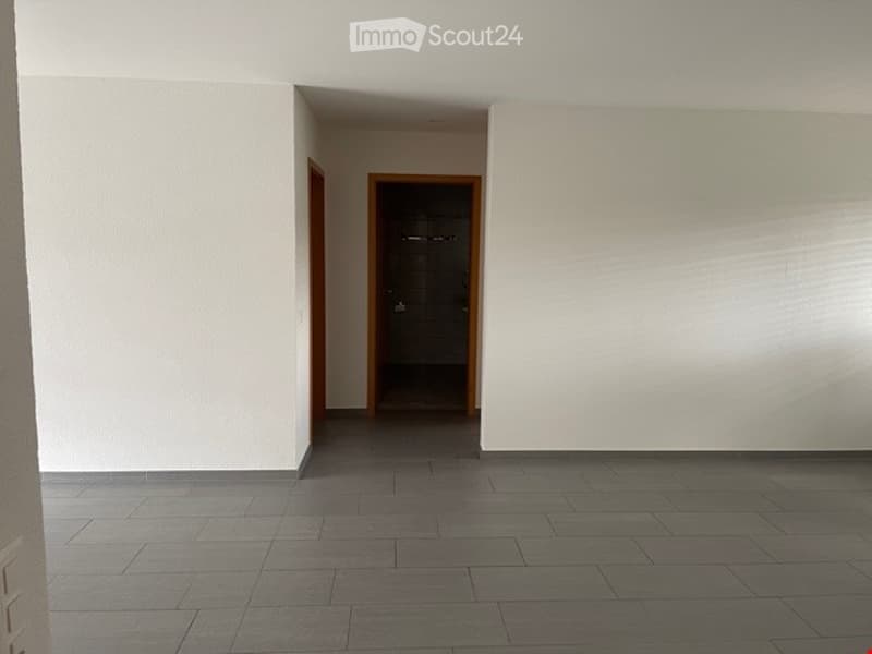 Empty room with white walls, grey tiled floor, and two doors leading to other spaces.