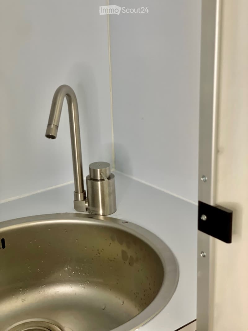 Modern stainless steel sink with a sleek, curved faucet and soap dispenser, mounted on a light blue wall.