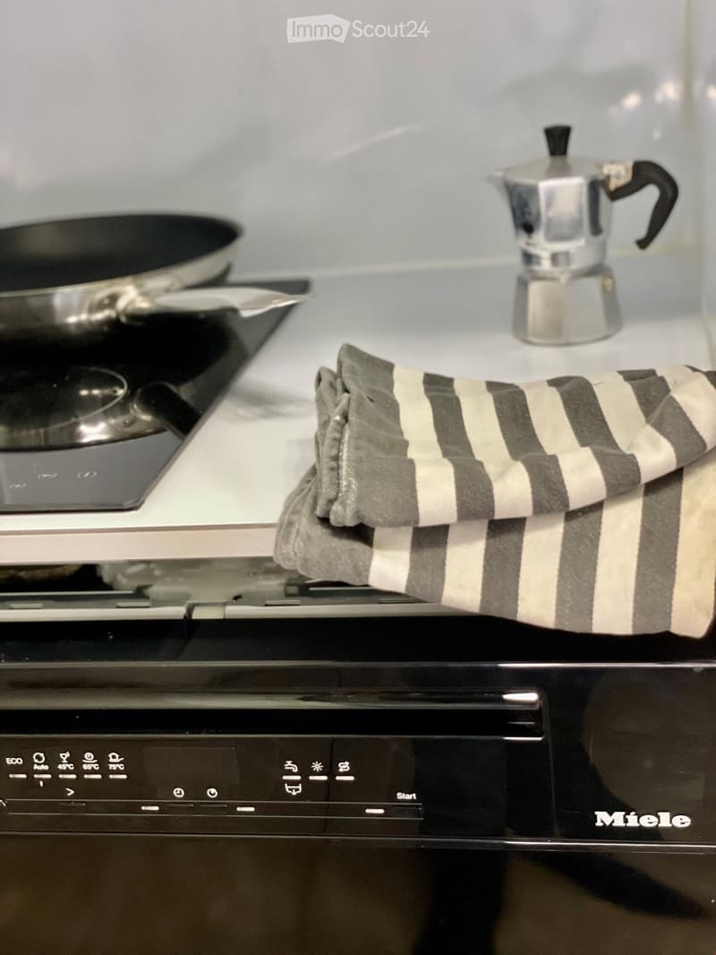 Modern kitchen with a black oven, frying pan, coffee maker, and an oven mitt on the counter.