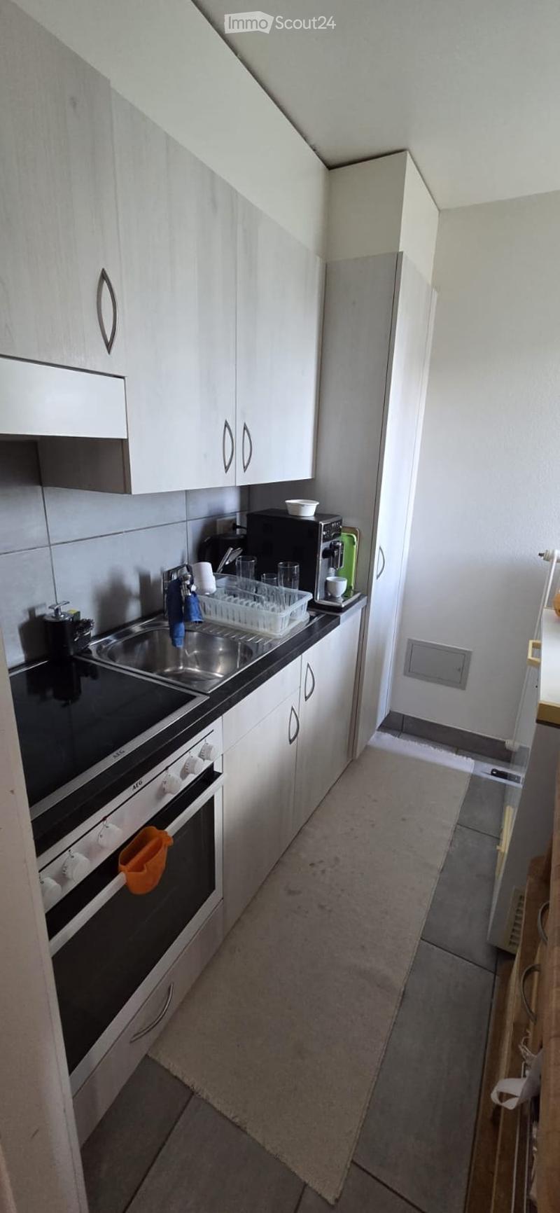 Modern kitchen with white cabinets, stainless steel sink, oven, coffee maker, and dish rack. The space features a black countertop and tiled backsplash.