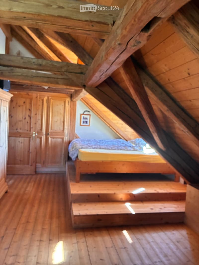 Cozy attic bedroom with wooden beams, slanted ceiling, wooden bed, and wardrobe.