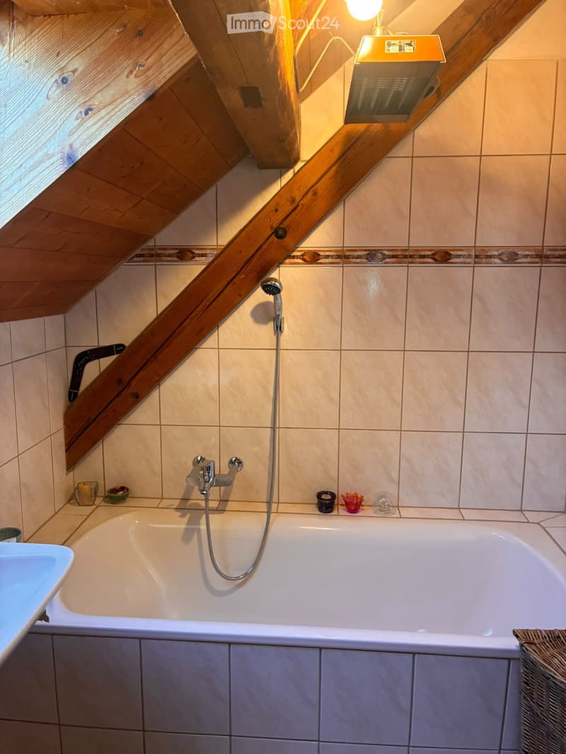 Bathroom with a bathtub, showerhead, faucet, sink, and decorative items on the edge of the tub.
