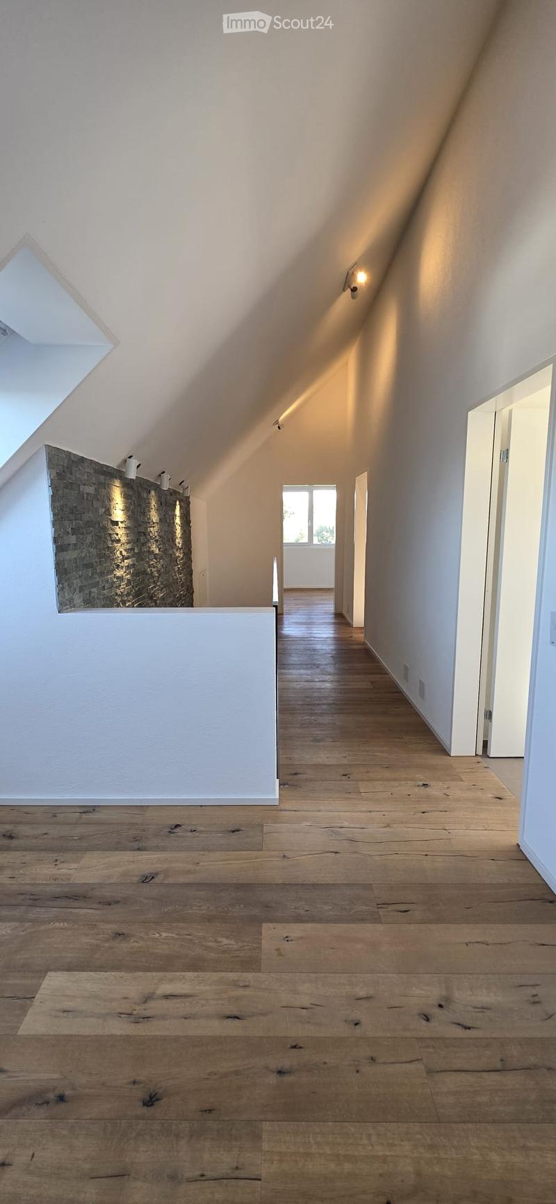 Empty hallway with wooden flooring, white walls, and recessed lighting. Features a skylight and a window at the end.