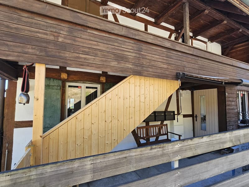 Wooden balcony with exposed beams, a chair, and a view of the building entrance.