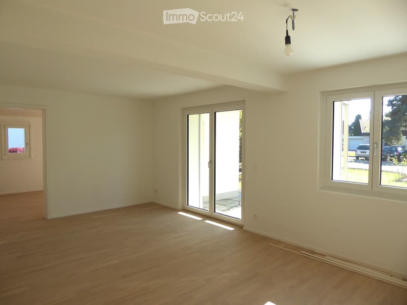 Empty room with wooden flooring, white walls, large sliding glass doors, and windows letting in natural light.