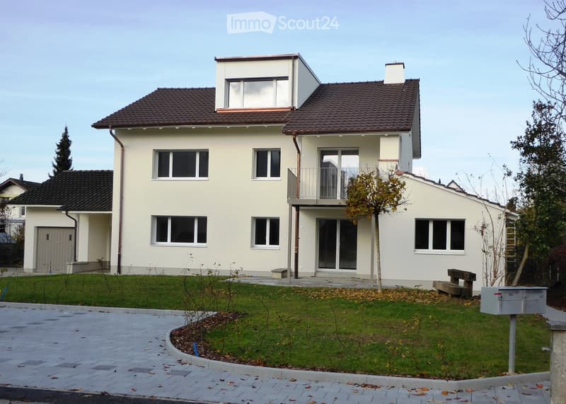Two-story house with a modern design, featuring a balcony on the upper level, multiple windows, and a well-maintained lawn.