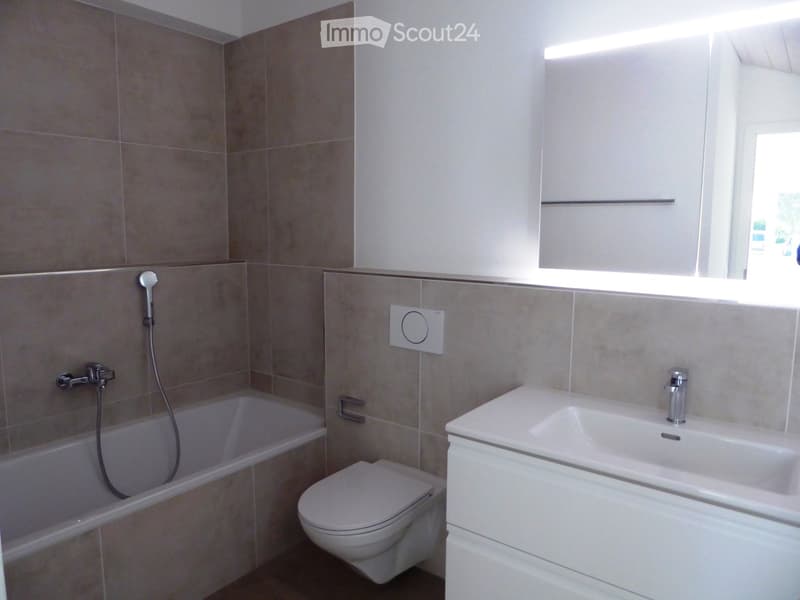 Modern bathroom with beige tiled walls, a bathtub, a toilet, a sink with a modern faucet, and a large mirror above the sink.